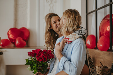 Young loving couple embracing and holding red roses bouquet while celebrating Valentines day at home