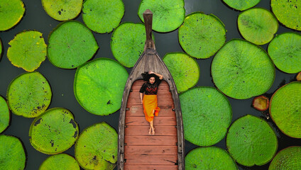 Obraz premium Aerial view of an Asian woman relaxing on a boat outdoor on Lotus pond at Phuket Thailand