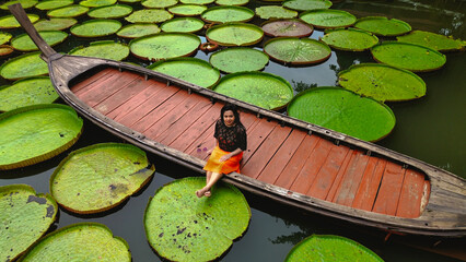 Girl sitting on a long tail boat surrounded by Queen Victoria water lilies in Phuket Thailand