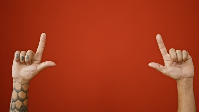 Isolated shot of tattooed adult man's hands, his finger pointing up over the blank space in an vivacious red background. no people around. side view reveals the hispanic male's raised hands.