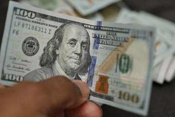 A close-up of a hand holding a new one hundred US dollar bill