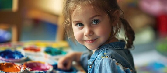 Joyful child using watercolor paints in kindergarten art class and gazing at the camera.