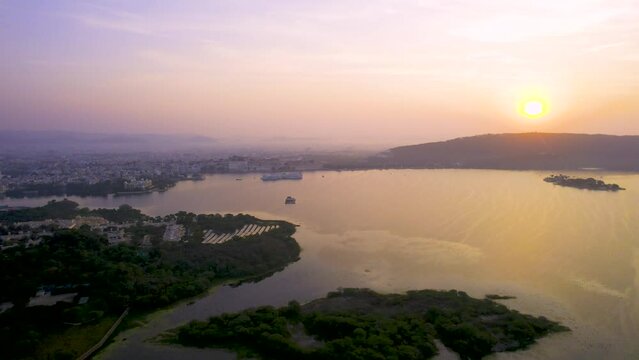 aerial drone shot flying sideways at sunrise over cityscape of udaipur rajasthan India towards lake pichola fateh sagar with sun rising behind aravalli mountains in this tourist spot