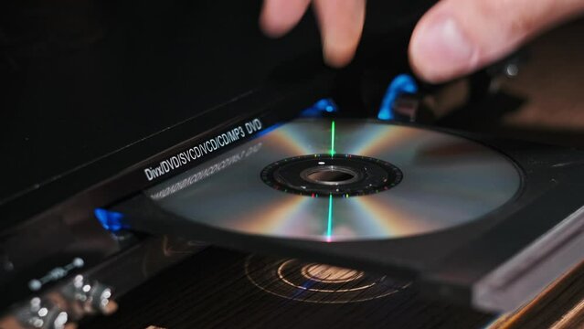 DVD compact disc is inserted into the player. Male hand loads CD into a CD player tray close-up. Music, movies, or data recorded on a laser optical information storage medium. Loading Compact Disc