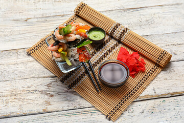Bowl with tasty sushi cones, ginger, wasabi and soy sauce on light wooden background
