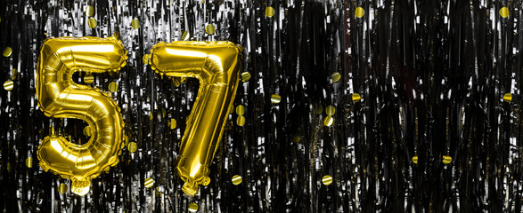 Gold foil balloon number number 57 on a background of black tinsel decoration. Birthday card,...