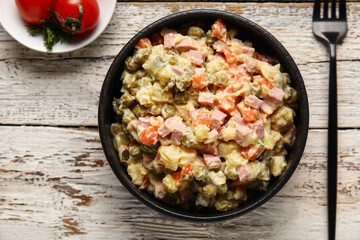 Bowl of tasty Olivier salad on light wooden background, closeup