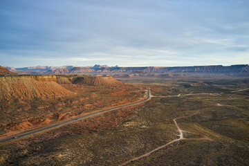 Naklejka premium An aerial shot of a road winding through a valley, surround by barrent desert, and rock cliffs.