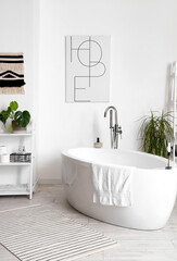 Interior of light bathroom with bathtub and green houseplants