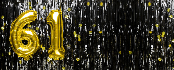 Gold foil balloon number number 61 on a background of black tinsel decoration. Birthday greeting...