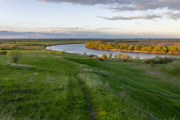 Colorful rural landscape with a path leading to a wide river, Lots of green grass in the foreground.