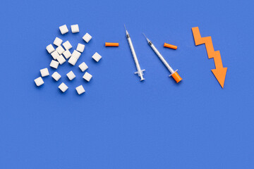 Sugar cubes with syringes for insulin injection and arrow directed downwards on blue background