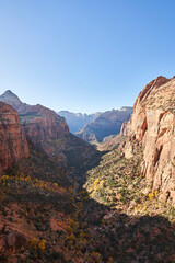 The inspiring view from Canyon Overlook in Zion National park. Shadows cover most of the valley, with a number of yellow trees seen below.