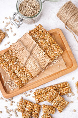 Board with tasty kozinaki, sunflower seeds and rope on white background
