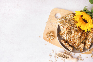 Board with bowl of tasty kozinaki, sunflower and seeds on white background