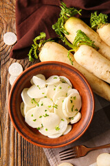 Bowl with slices of fresh daikon radish on wooden background