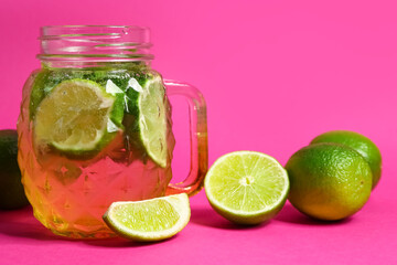Mason jar of cold mojito and lime on pink background