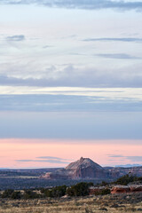 A large rock mountain stands out of the surrounding landscape and grassland, beautifully set against a colorful pink and purple sunset.