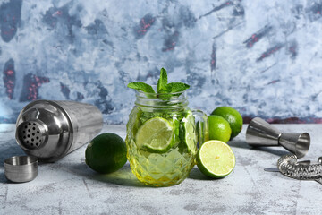 Mason jar of cold mojito and shaker with lime on blue table