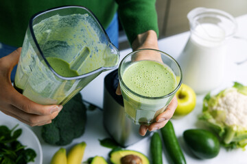 woman pouring homemade fresh green smoothie into a glass made from vegetables and fruits. healthy...