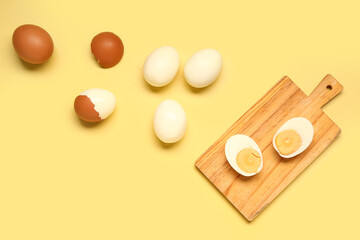 Fototapeta na wymiar Tasty boiled eggs and wooden board with halves on yellow background
