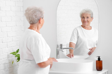 Senior woman looking in mirror at home - obrazy, fototapety, plakaty