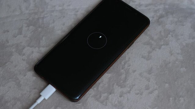 hands of a man turning on the charger to charge the smartphone battery. Low charge level on the smartphone screen. The phone is charged by connecting the wires