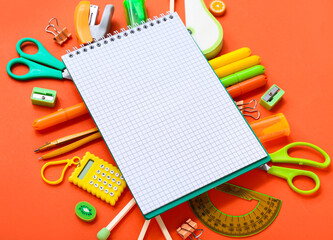 Notebook with different stationery supplies on orange background