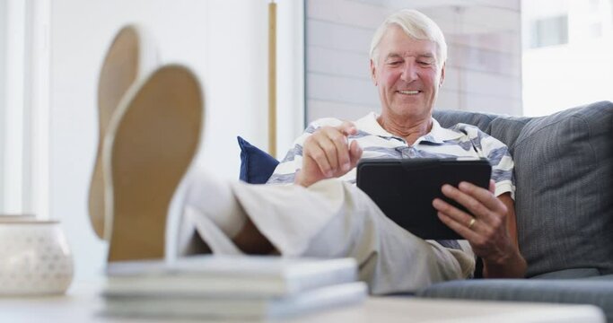 Tablet, relax and senior man on a sofa with social media, search or ebook in his home. Smile, face and old male person with digital, app or online shopping, reading or streaming in a living room