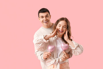 Happy young couple with heart-shaped air balloons on pink background. Valentine's day celebration