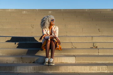 Afro-american lady with grey afro hair relaxing in the sun in city