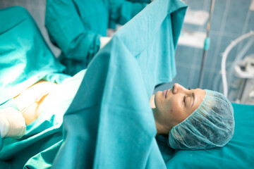 Female patient lying on operating table during surgery covered with sheets.