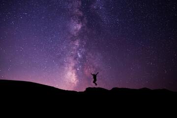 Silhouette of a hiker jumping  on the hill, on the milky way galaxy background.