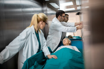 Two medical professionals male and female with sleeping patient on a gurney in elevator.