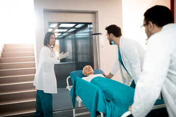 Medical team rushing sick elderly woman lying on medical gurney in hospital elevator. - obrazy, fototapety, plakaty