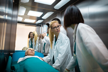 Two female doctors talking in elevator while moving elderly female patient on a gurney with their colleague.