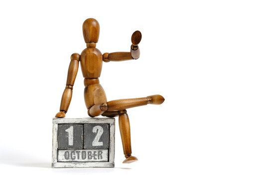 October 12, wooden calendar with mannequin sitting on it on white background. Calendar date.