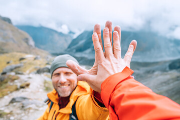 Smiling backpacker dressed orange jacket giving High Five to female mate during Himalaya valley...