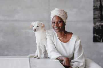 Smiling woman in a turnban sitting with a white dog by her side. African girl in traditional attire...