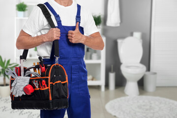 Plumber with bag of instruments showing thumbs up in bathroom, closeup. Space for text