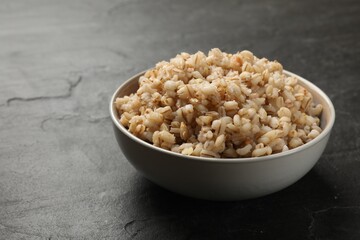 Tasty pearl barley porridge in bowl on dark textured table, closeup. Space for text