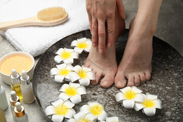 Obraz na płótnie Canvas Woman soaking her feet in bowl with water and flowers on light grey floor, closeup. Spa treatment