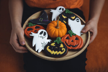 Little kid in orange t-shirt holding wooden plate with homemade delicious Halloween gingerbread cookies. Trick or treat. Handmade ghost, jack lantern, pumpkin, creepy spooky biscuits. Close-up, macro