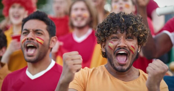 Close camera view of Hispanic friends cheering loudly on stadium. Starting to clap and shout from being happy of game outcome. Supporting Spain national team and painting Spanish flags on their faces.