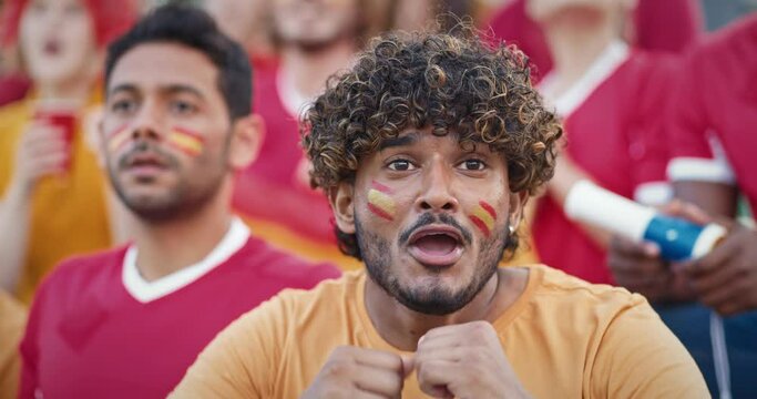 Close up shot of Hispanic Male with curly hair holding his hands together as showing his emotions at stadium tribunes. Afterwards starts yelling and shouting as being happy from game outcome.