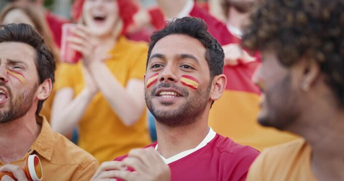 Group of Multi-ethnic friends cheering on stadium tribunes for Spain national team. Yelling and shouting at sports event to support favourite team. Spanish flags painted on faces.