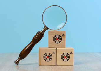 Wooden cubes with a drawn target and a magnifying glass on a blue background, symbolizing the...