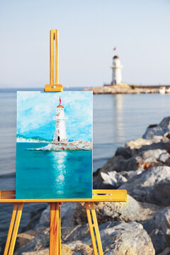 Acrylic painting depicting the white lighthouse in Alanya, Turkiye. Beautiful picture on canvas standing on the wooden easel. Life drawing art concept. Selective focus. Blurred background.