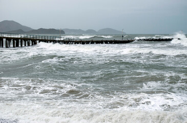 Winter storm at sea in Koktebel. Big waves and storm clouds. Waves with white foam break on the pier.
