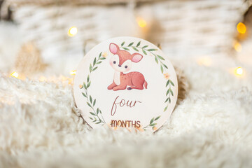 Milestone disc with a cute deer, flowers and writing saying ''four months'' placed on a white...